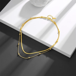 Détail d'un collier double rang en or avec chaîne serpent et perles sur support blanc