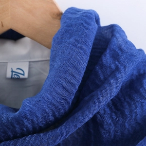 Macro shot of blue crinkled cotton scarf texture with brand tag on wooden hanger