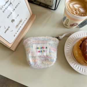 Mini striped fuzzy knit makeup bag with embroidered label and zipper in cafe setting