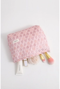 Detail of pink canvas makeup bag with 3D heart pattern and woven brand label