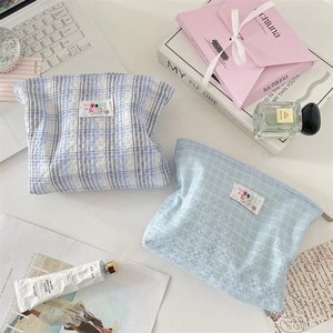Close-up of blue plaid cotton makeup bags with embroidered label in a desktop setting