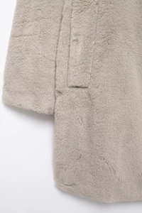 Detailed close-up of light beige faux fur coat texture showing soft plush fabric and pocket flap