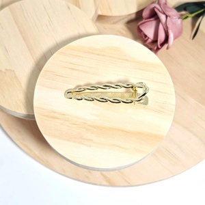 Detailed close-up of golden twist rope metal hair clip on a wooden display stand