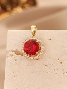 Macro shot of gold four-prong pendant with red round zircon and white halo stones