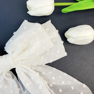 Detail of white tulle bow hair clip with textured polka dots on black leather surface