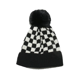 Close-up of black and white checkerboard knit beanie with a faux fur pompom on white background
