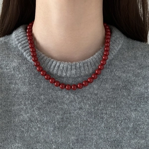 Détail d'un collier de perles rouges sur un pull gris pour un style vintage français