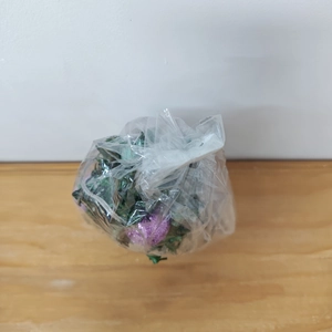Detailed view of artificial green leaves with purple glitter inside plastic wrapping