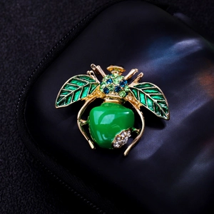 Macro view of a gold insect brooch with a green enamel apple body and colorful rhinestones