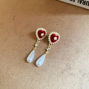 Detail of red heart earrings with golden flower relief and white teardrop pearls