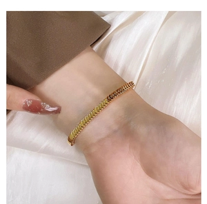 Close-up of golden scale textured bracelet on wrist with elegant fabric background
