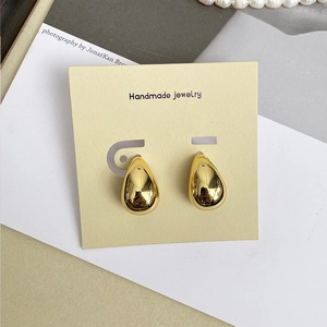 Detail shot of golden water drop earrings with mirror finish on display card