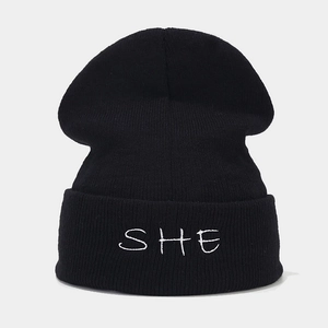 Detailed view of white SHE embroidery on a black ribbed knit beanie cuff