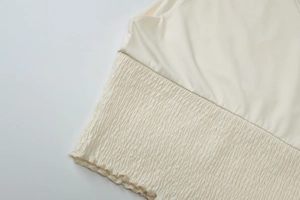 Detailed close-up of cream-white fabric showing pleated texture and refined stitching
