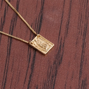 Macro shot of gold rectangle pendant with religious figure engraving on a box chain