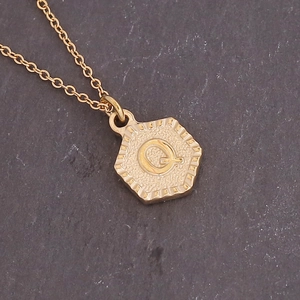 Detailed macro view of a gold hexagonal pendant with a textured letter Q on rock background