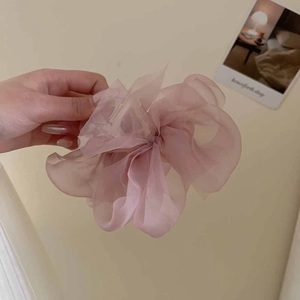 Detail showing a large pink tulle flower hair claw clip held against a neutral background