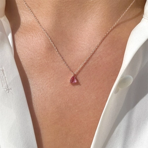 Close-up of pink heart-shaped crystal pendant on a thin gold chain worn by a model