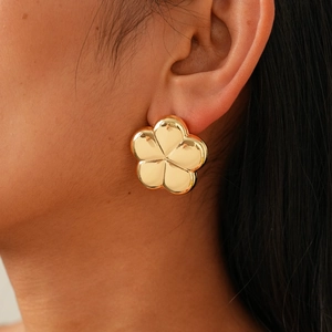 Close-up of a model wearing large polished gold flower stud earrings in a minimalist style
