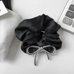 Detailed shot of a black satin hair scrunchie featuring a silver metallic bow decoration