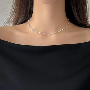 Detail view of a 925 silver beaded necklace with a minimalist cross pendant on a model