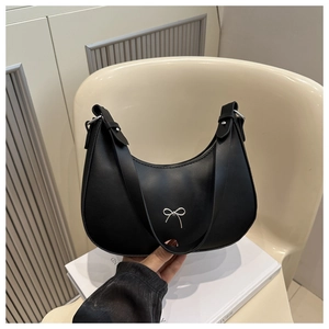 Detailed macro view of black leather crescent bag featuring a silver metal bow accent