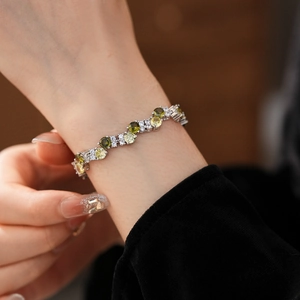 Close-up of a silver twisted zircon bracelet with green and white gems on a model's wrist