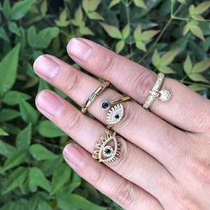 Detail of four gold fashion rings with evil eye charms and colorful crystals on hand
