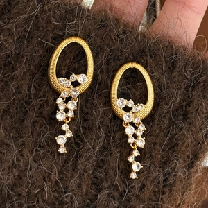 Boucles d'oreilles franges dorées avec cristaux clairs sur un tissu doux texturé