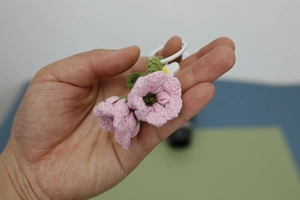 Macro detail of hand-knitted pink lily of the valley flower keychain with green leaves
