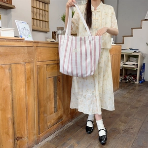 Detail of red striped canvas tote bag with woven label shown in a vintage shop setting