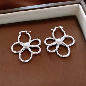 Detailed macro view of silver hollow flower earrings with a textured surface and pearl
