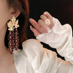 Detailed view of vintage gold leaf earrings with long dark red beaded tassels on model