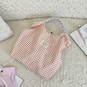 Détail du sac cabas à carreaux rouges avec poignée en corde à pois et écusson de marque