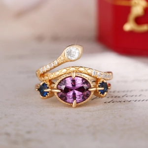 Close-up of golden snake ring with purple gemstone and blue accents on vintage paper