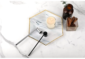 Flat lay of stainless steel candle snuffer and wick hook on a marble tray with candle