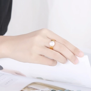 Detail of a large white pearl on a gold stainless steel ring worn by a model