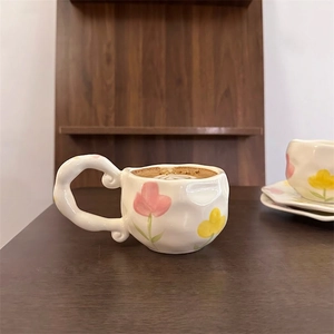 Detail of a handmade ceramic coffee cup with pink tulip painting and a wide curved handle