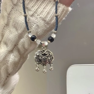 Macro detail of silver longevity lock pendant with beads and blue woven cord strap
