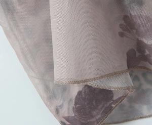 Detailed macro shot of taupe floral mesh fabric with professional overlock stitching finish