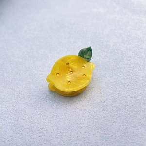 Detail of a bright yellow lemon acetate hair clip with green leaves on a grey surface