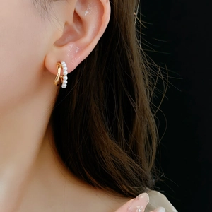 Detail of C-shaped double hoop earring with gold finish and small pearls on model