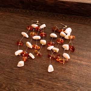 Dettaglio di orecchini con frange in perle acriliche ambra e crema su legno marrone