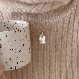 Macro detail of irregular sterling silver pendant with engraving on beige sweater background