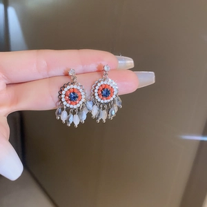 Detail of silver drop earrings featuring blue crystals and coral bead tassels on a hand