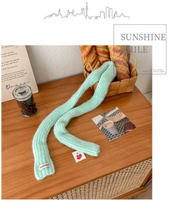 Close-up of light green knit scarf with VEGETABLE label on a warm wooden tabletop