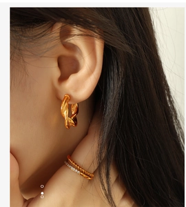 Detail view of gold twisted C-shape hoop earrings on model with high gloss finish