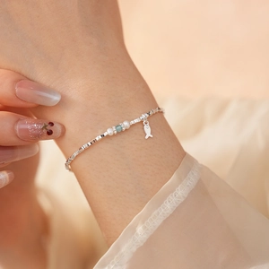 Detailed shot of silver fish charm bracelet with white pearls and blue bead on wrist