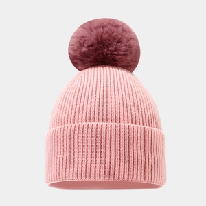 Detail of pink knit hat featuring a large fluffy burgundy faux fur pompom and ribbed texture