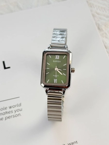 Close-up of square green quartz watch dial with silver metal link strap on white card